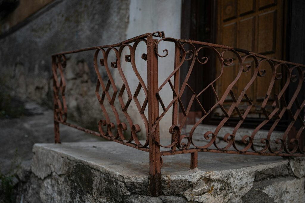 Rusted wrought iron railing on a stone porch in front of a door, needing restoration