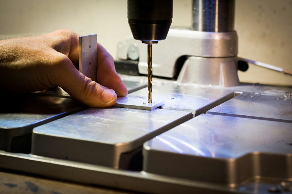 Operator's hand guiding a drilling machine on a metal bar in a workshop
